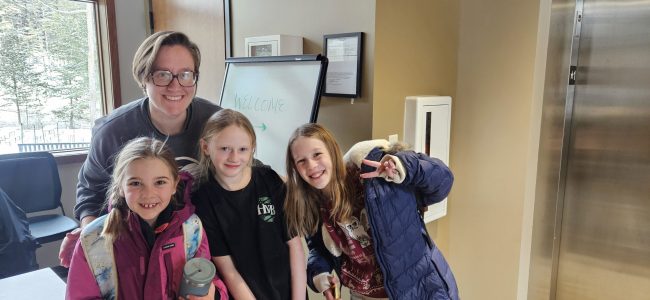 A woman poses with three young youth.