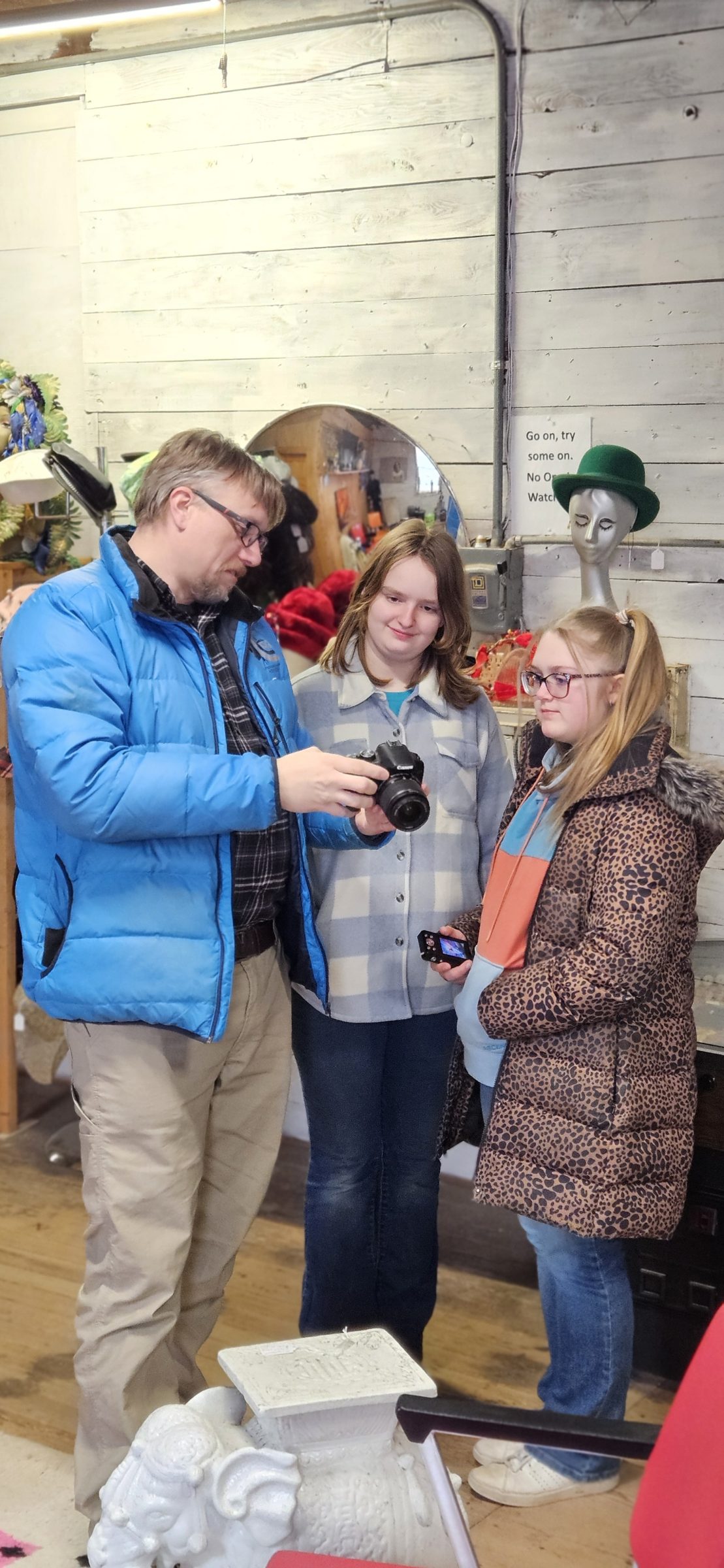 A man holds a camera for two teenagers to see how to change its settings.