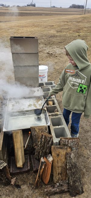 A youth transfers maple sap from one pan to the other as it boils down into syrup during a recent maple syrup workshop.